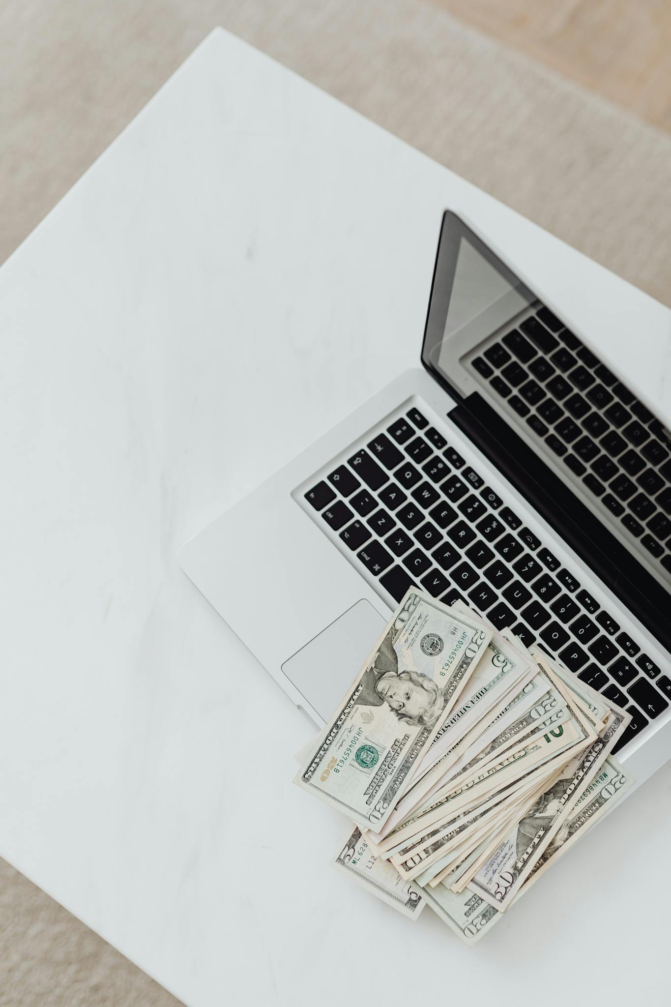 Overhead shot of a laptop with US dollar bills on a white desk. Concept of finance and technology.